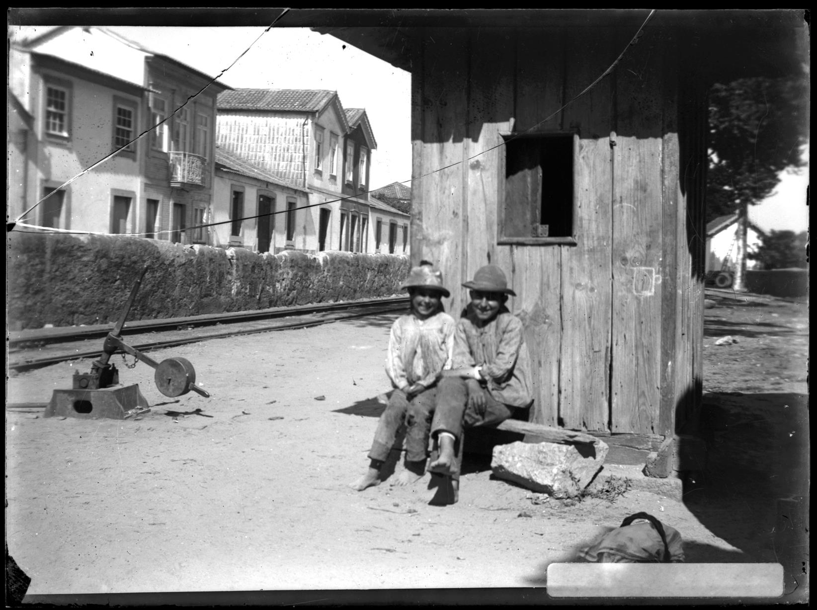 Crianças sentadas em frente a uma casota numa linha de caminho de ferro